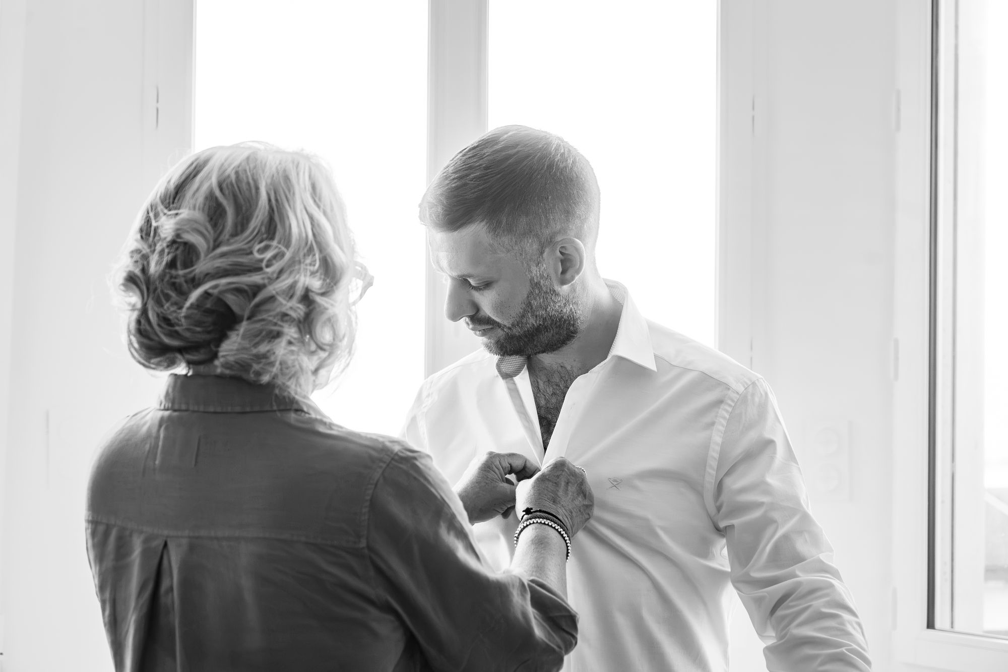 La mère du marié boutonne sa chemise, en noir et blanc