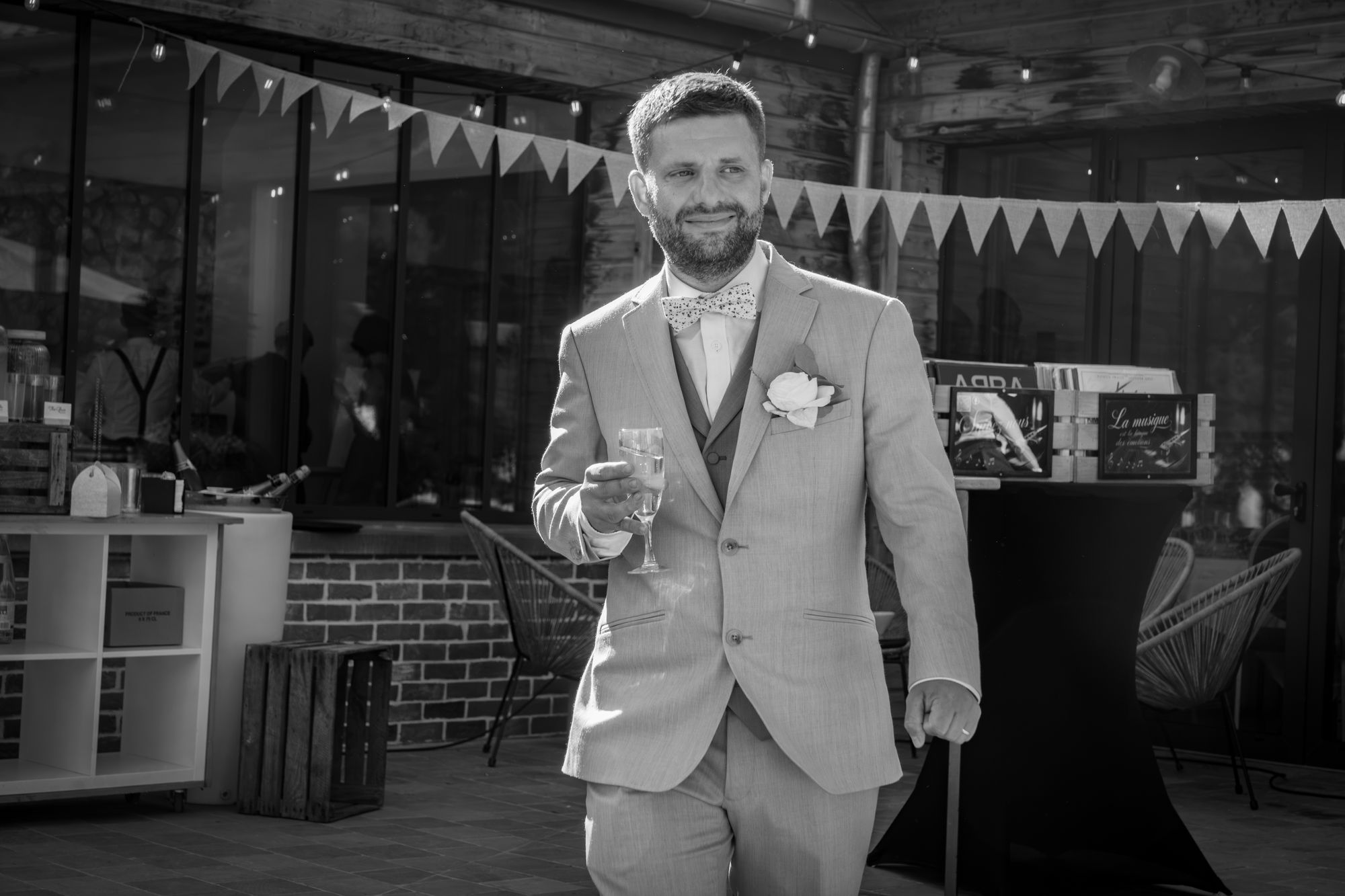 Le marié, coupe de champagne à la main, en noir et blanc